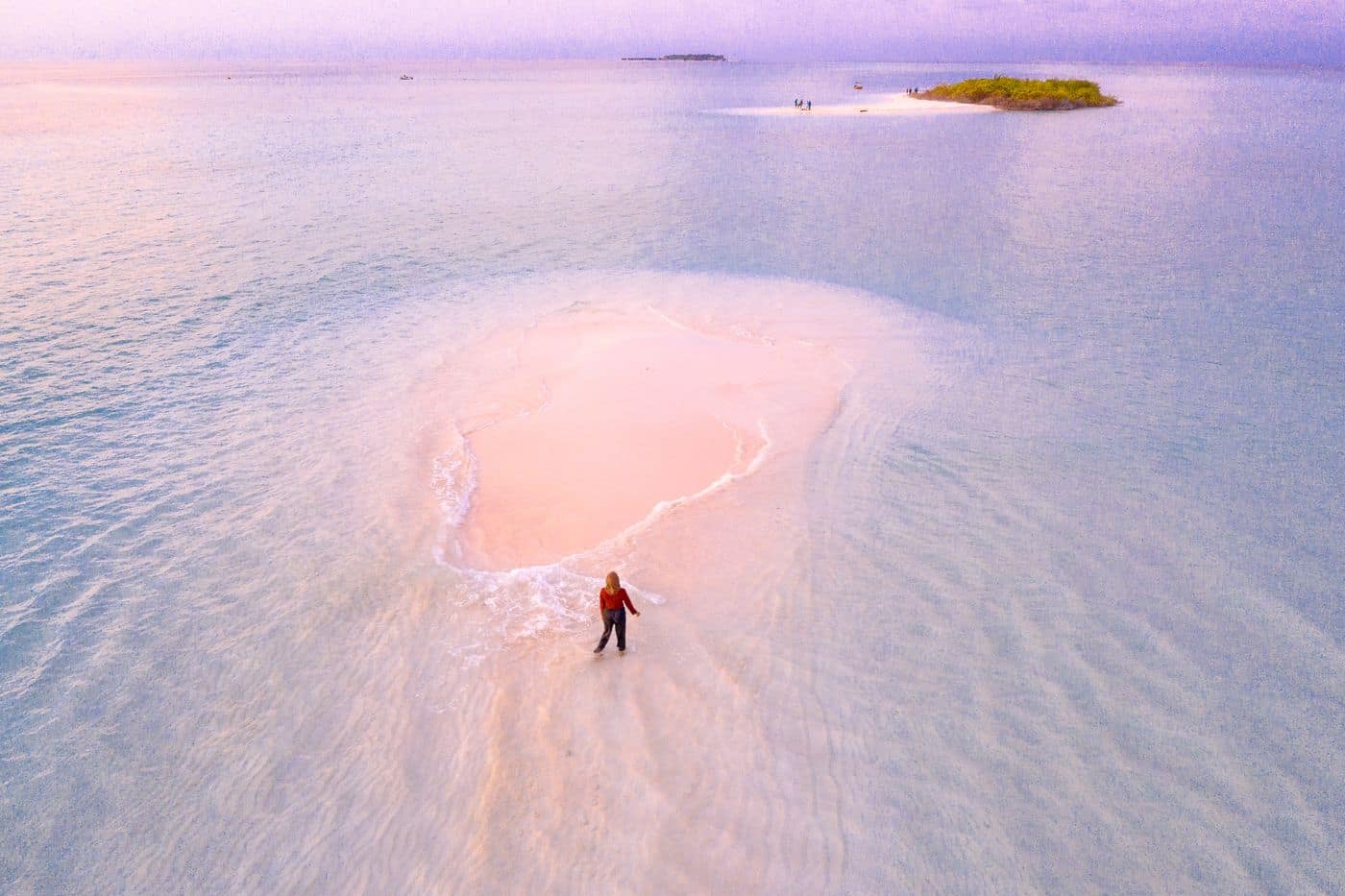 A person standing on a sandbar surrounded by open shallow water